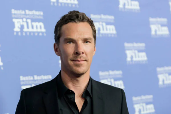 Benedict Cumberbatch de camisa e blazer preto posa com sorriso sem dentes - metrópoles