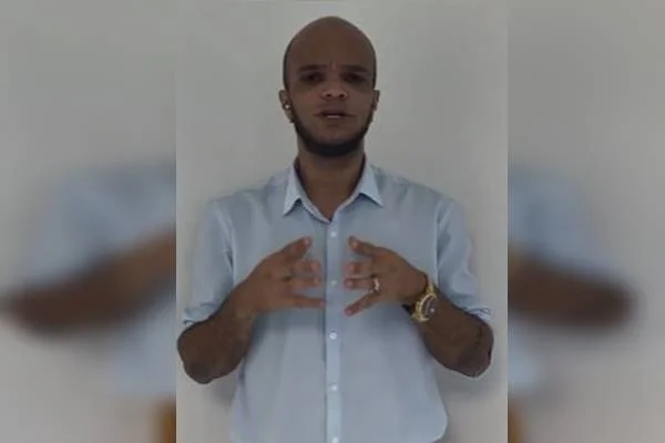 Fotografia colorida de homem com camisa branca faz gesto com as mãos