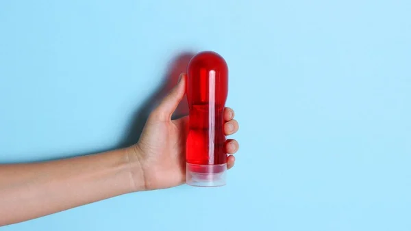 Mão segurando um recipiente com líquido vermelho em um fundo azul bebê
