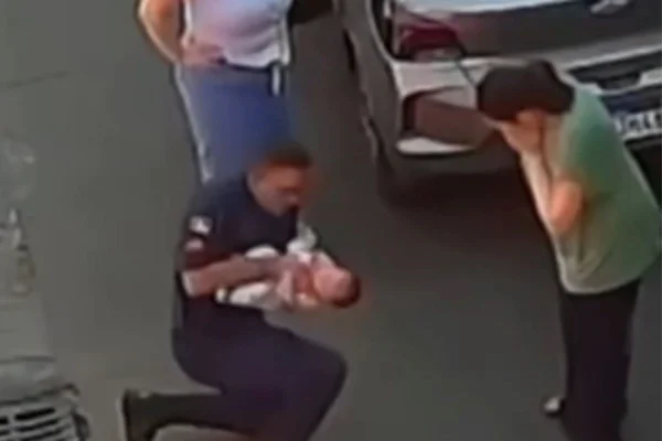 Foto colorida de bombeiro realizando manobra de desengasgo em bebê - Metrópoles
