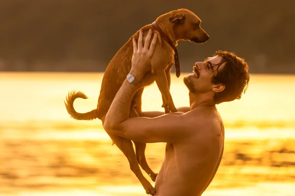 Imagem colorida de Rafa Vitti e o cachorro Amendoim em gravação no pôr do sol da praia para o filme Caramelo, da Netflix