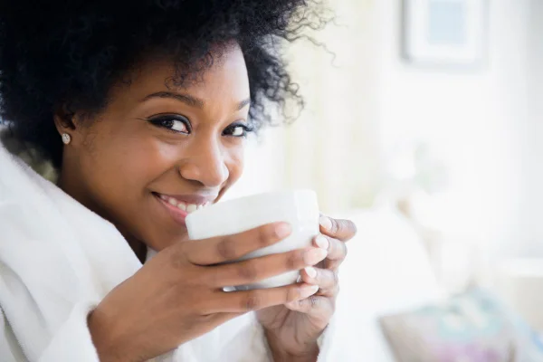 foto colorida mulher negra tomando chá e sorrindo