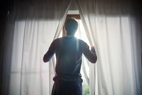 Foto de Homem abrindo cortinas no quarto - Metrópoles