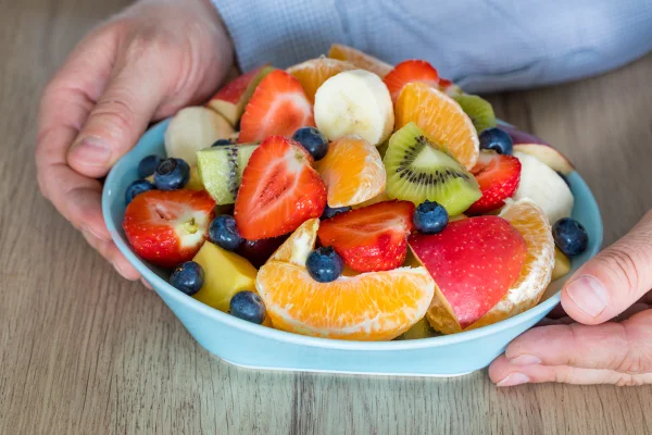 Foto colorida de mãos segurando uma tigela com frutas cortadas - Nutricionista lista melhores alimentos para quem tem intestino preso - Metrópoles