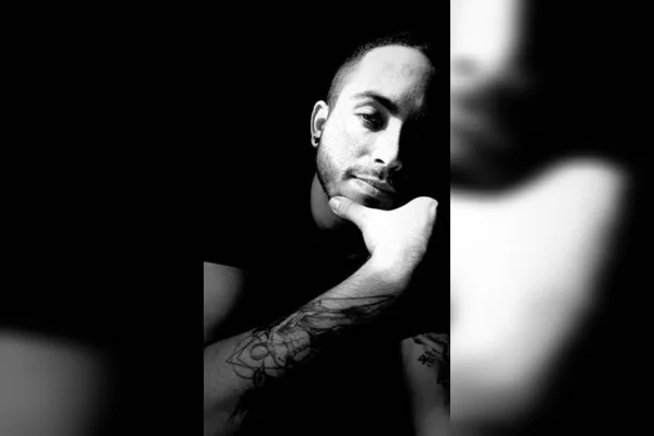 Foto mostra jovem de barba e corpo tatuado em primeiro plano olhando diretamente para a câmera - Metrópoles