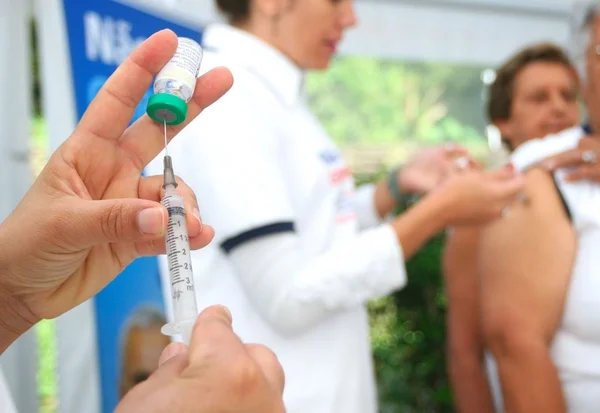 foto colorida, em primeiro plano enfermeiro segura seringa de vacina da gripe; um pouco adiante, enfermeiro com jaleco aplica vacina em pessoa - Metropoles