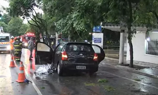 Imagem colorida mostra um carro preto com porta aberta e um corpo coberto no chão de um homem que morreu eletrocutado durante a tempestade em São Paulo - Metrópoles