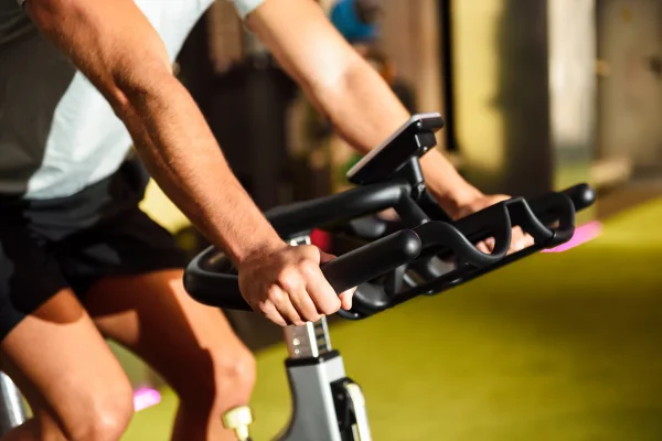Mãos de um homem treinando em uma academia, praticando ciclismo indoor. Conceito de esporte e fitness. Metrópoles