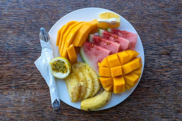 Frutas tropicais em um prato de café da manhã, close-up. Melancia fresca, banana, maracujá, abacaxi, jaca, manga, mamão e laranja para comer em restaurante de praia, ilha de Zanzibar, Tanzânia, África