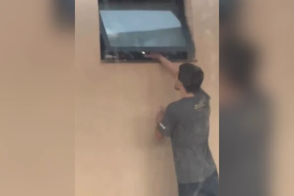 Imagem colorida de homem gravando mulher pela janela do banheiro. Metrópoles