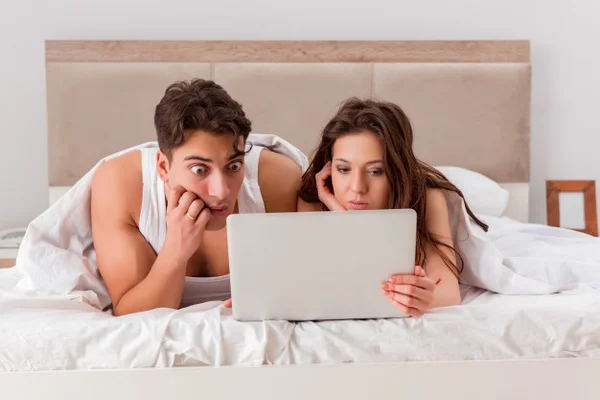 Homem e mulher mexendo no computador em cima da cama