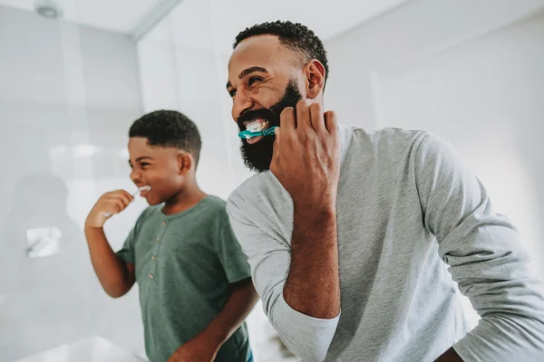 Pai ensinando filho a escovar os dentes Quando começar a escovar os dentes? Um guia da saúde bucal na infância