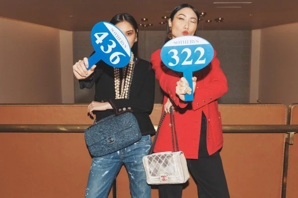 Duas mulheres usando roupas e bolsas da Chanel exibem placas de leilão - Metrópoles