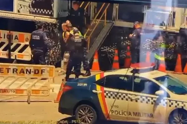 Viatura da PM parada, policiais ao fundo, escada e cones
