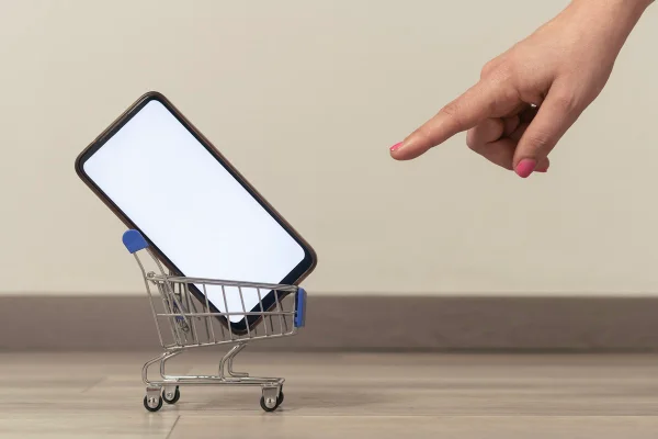 Na imagem com cor, dedo aponta para um carro de compras que tem um celular - Metrópoles