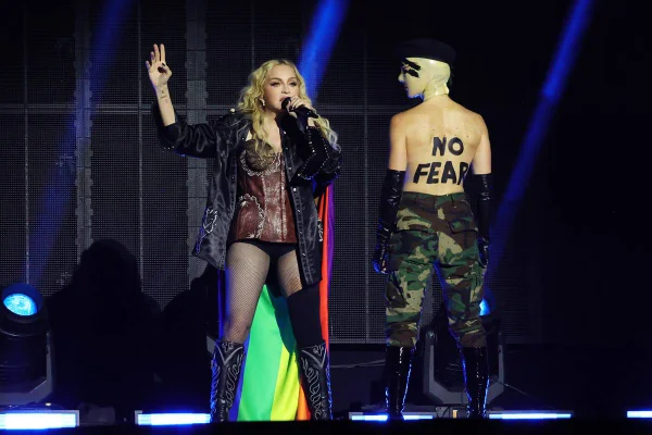Foto colorida de Madonna cantando no palco com uma bandeira LGBTQIA+