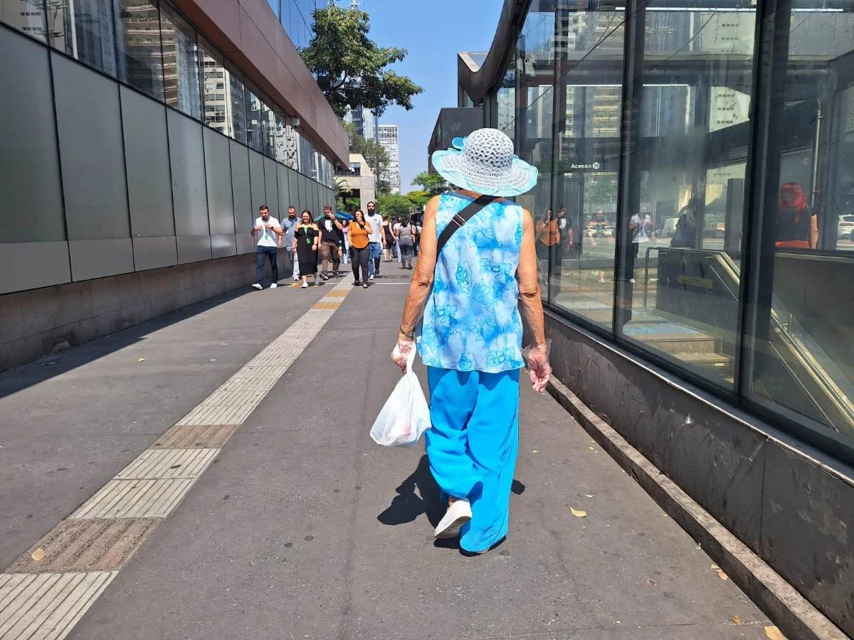 Mulher caminha de chapéu sob sol em trecho da Avenida Paulista
