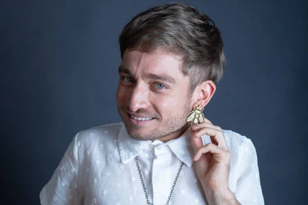 foto colorida de homem loiro com nanismo de camisa branca e brinco dourado - metrópoles