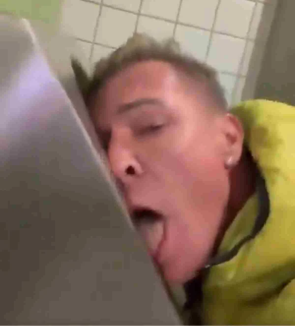 Imagem colorida. Homem com camisa amarela lambendo vaso sanitário