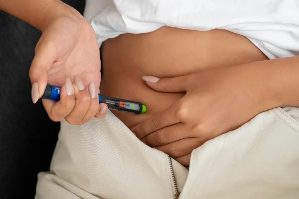 Foto colorida de mulher aplicando caneta emagrecedora no abdômen - Metrópoles