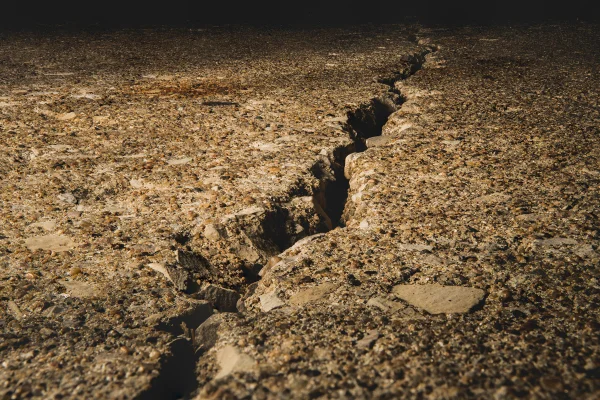 Um solo rachado coberto de pedras sob a luz do sol, com um fundo desfocado. Metrópoles