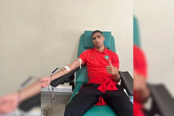 Imagem colorida de homem vestido em blusa Vermelha com símbolo de Marrocossentado em poltrona enquanto doa sangue - Metrópoles