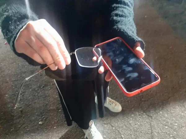 Mulher mostra óculos e celular quebrado após ser abordada e agredida com o marido por morador de rua e oito ladrões em Curitiba, Paraná - Metrópoles