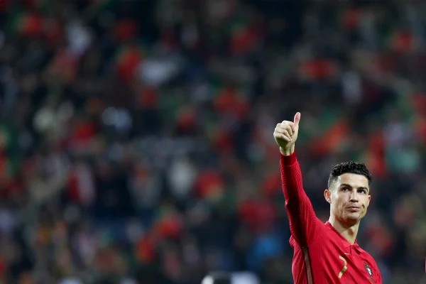 O jogador português Cristiano Ronaldo. Ele olha para a arquibancada de um estádio e dá um sinal de joia com a mão, usando o uniforme da seleção de Portugal. Em segunda plano é possível ver os torcedores - Metrópoles