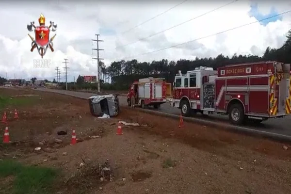 carro prata tombado no acostamento com caminhão dos bombeiros ao lado