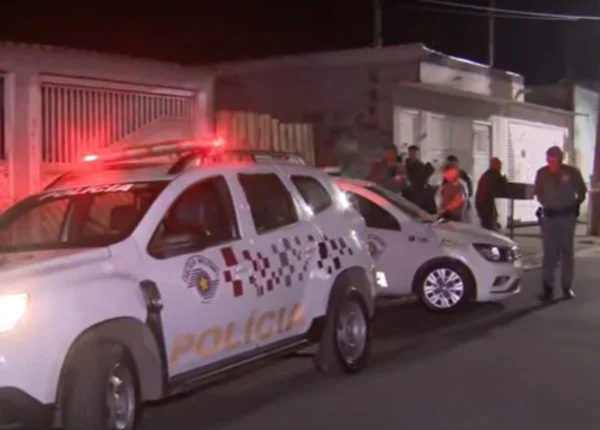 Foto colorida mostra viaturas da polícia estacionadas em frente a casa onde morava vítima de homicídio