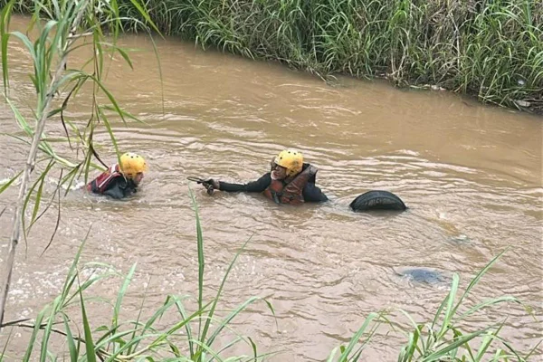 Imagens coloridas mostram bombeiros com capacete amarelo dentro de rio e o pneu de um carro que está submerso
