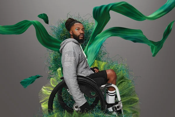 Campanha de divulgação dos moletons da marca Malwee, feitos a partir de um fio reciclado. Posa para foto um modelo negro, com cabelos de tranças, sentado em uma cadeira de rodas. Ele veste um moletom cinza e uma bermuda preta com meias cumpridas brancas.