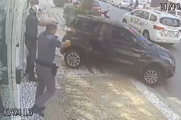 Imagem colorida de carro preto andando e policiais apontando arma ao veículo. Metrópoles