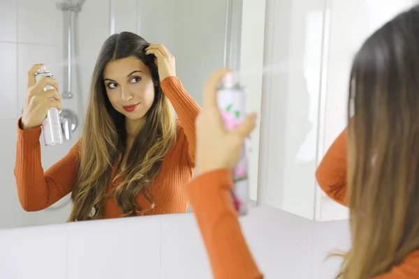 Mulher jovem aplicando spray no cabelo de frente ao espelho