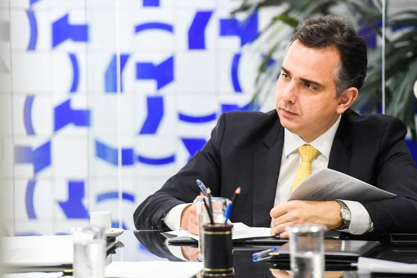 O presidente do Senado, Rodrigo Pacheco. Ele assina documentos, olhando para frente, num dos salões do Congresso Nacional - Metrópoles