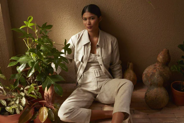 Foto de divulgação da nova coleção de roupas da marca Dafiti. Na foto, modelo posa com itens da etiqueta. É um mulher jovem, de pele morena e cabelos longos, lisos e pretos, que veste top, casaco e calça, tudo bege, em tecido de linho cru.