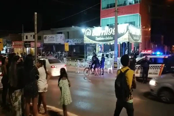 Foto colorida. Multidão observa corpo de homem morto a tiros