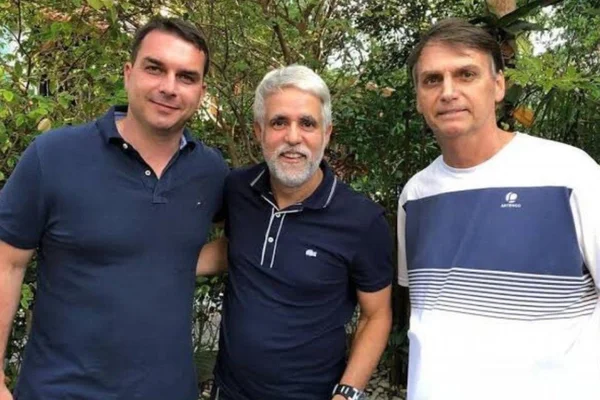 O senador Flávio Bolsonaro, o pastor Cláudio Duarte e Bolsonaro posam para foto em encontro. No fundo aparecem folhagens, e todos usam camiseta esportiva - Metrópoles