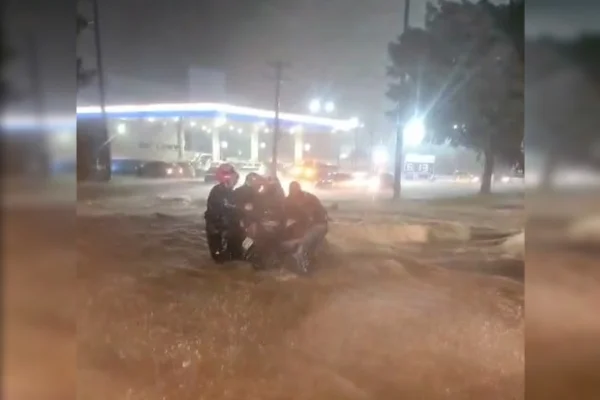 Imagem de diversos motociclistas juntos em meio a uma enxurrada, tentando segurar uma motocicleta