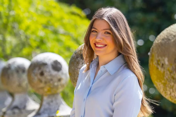 Foto colorida de mulher com cabelo longo. Ela está sorridente e próximo a um jardim - Metrópoles