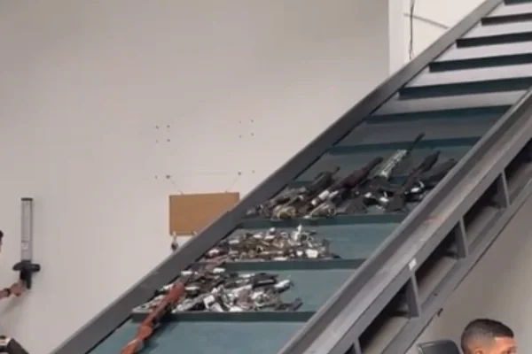 Imagem colorida de armas apreendidas em uma esteira sendo destruídas - Metrópoles