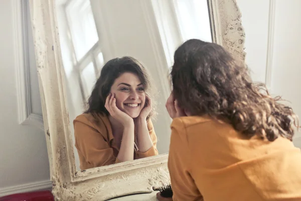 Imagem colorida de uma mulher sorrindo ao espelho - Metrópoles