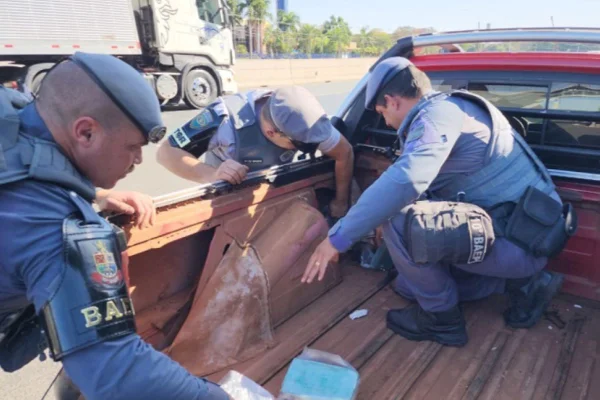 Policiais fardados revistam caçamba de caminhonete