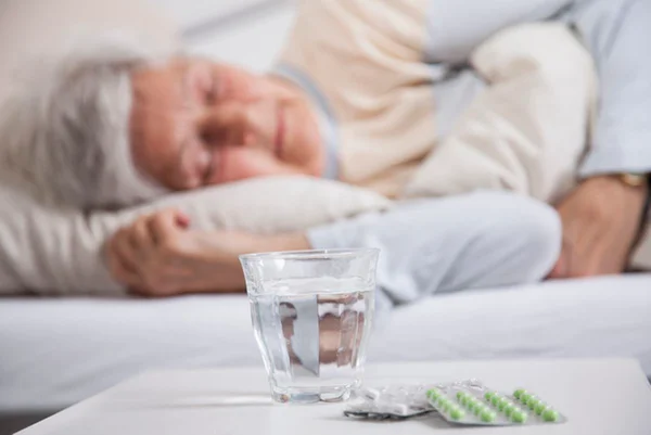 Foto de idosa dormindo atrás de copo de água e cartela de remédio/medicamentos - Metrópoles