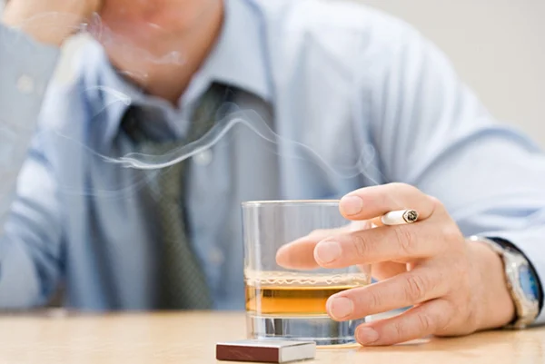 Homem de camisa social com cigarro e copo de bebida na mão - Metrópoles