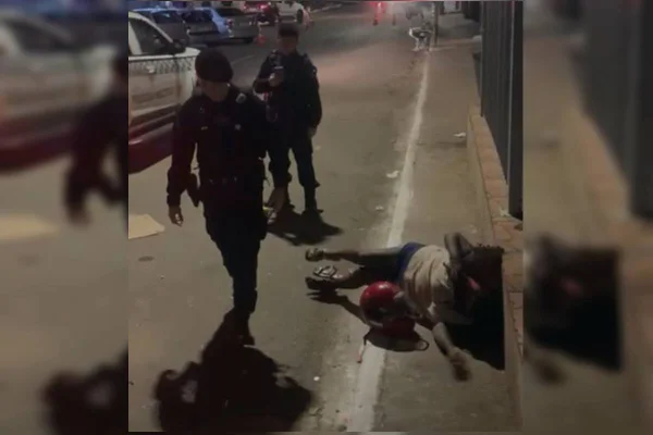 Foto colorida que mostra dois policiais militares e uma mulher caída no chão durante uma abordagem