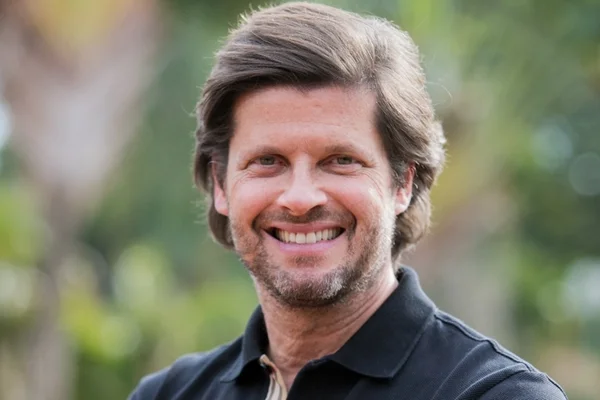 Foto colorida de um homem branco, de olhos claros e sorridente