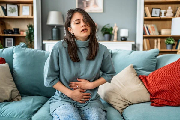 Foto colorida de mulher sentada em sofá. Ela está com as mãos na barriga - Metrópoles