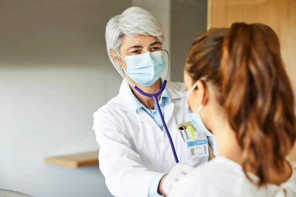 Foto de uma médica examinando uma moça jovem com o cabelo amarrado