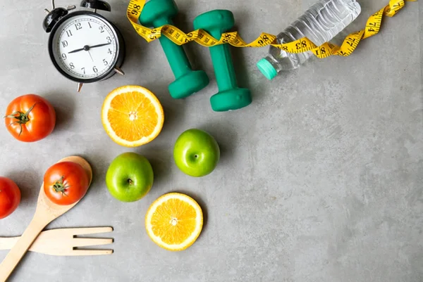 Foto com relógio, frutas, garrafa de água, fita métrica e talheres - Metrópoles